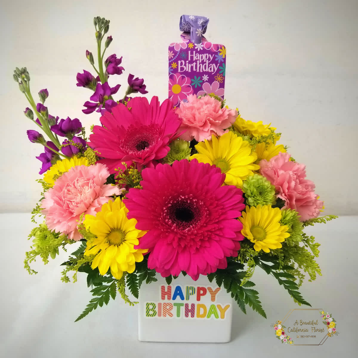 Bright mixed flower arrangement in a white birthday container