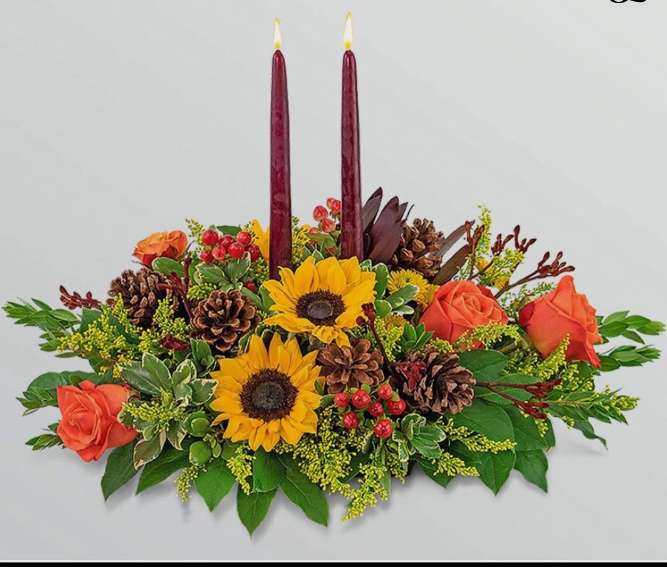 Autumn floral centerpiece with sunflowers, orange roses, and two burgundy candles