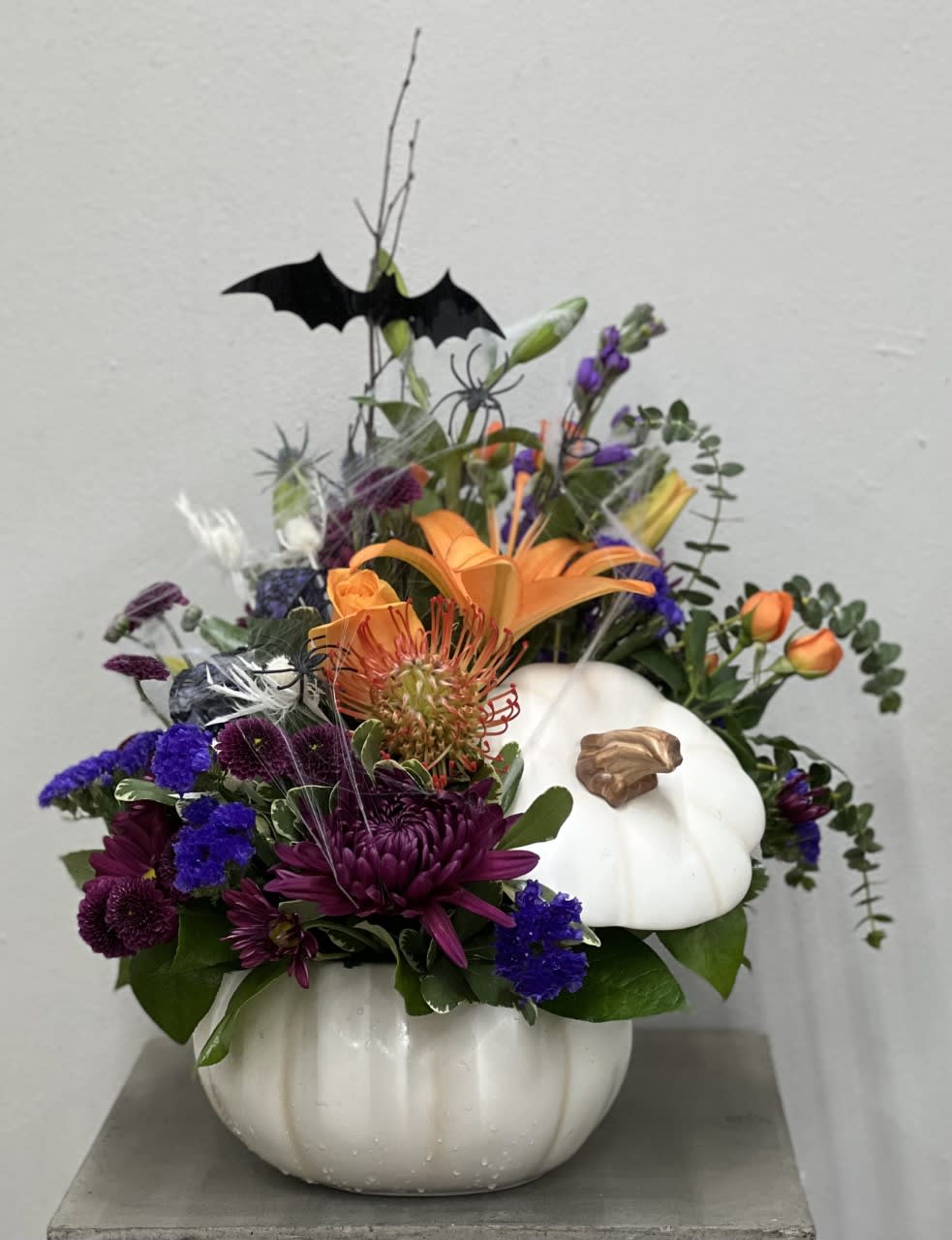 Halloween floral arrangement in a white pumpkin container with a bat topper