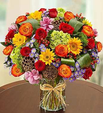 Colorful bouquet of roses, sunflowers, and small purple flowers in a glass vase
