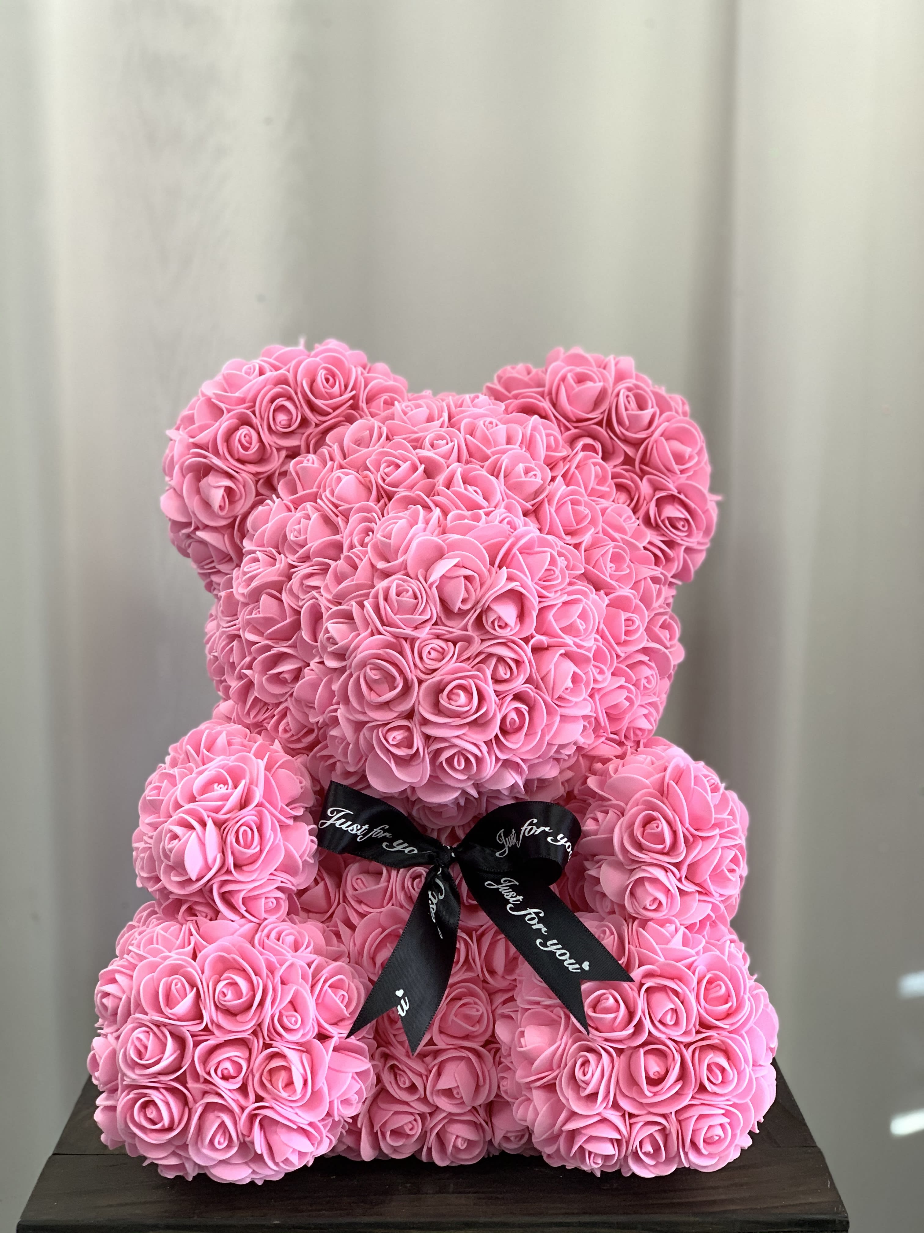 Pink teddy bear made of roses with a black ribbon