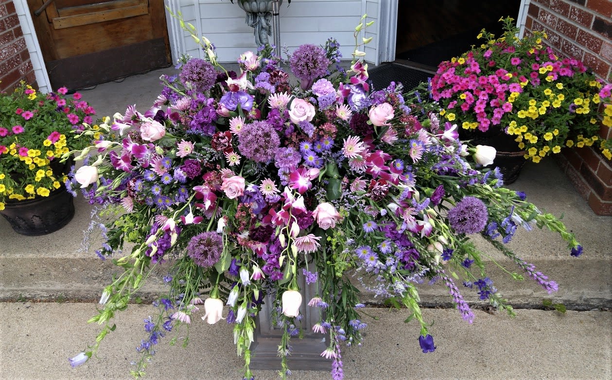 Large cascading arrangement of purple and pink flowers on a low pedestal.