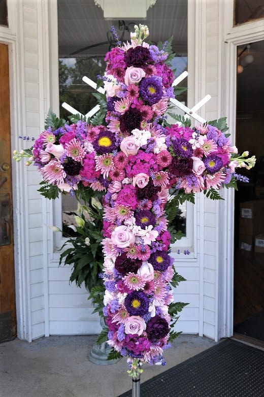 Tall cross-shaped standing spray of pink and purple flowers on a metal stand.