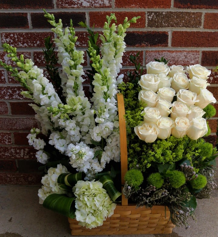 Tall white snapdragons and roses arranged with green accents in a woven basket