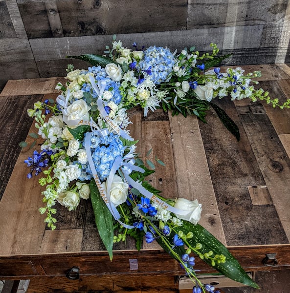 Long blue and white floral spray with ribbons arranged on a wooden surface