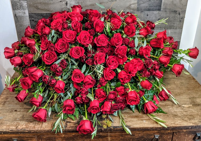 Large mound of red roses arranged in a low cascading display on a wooden surface