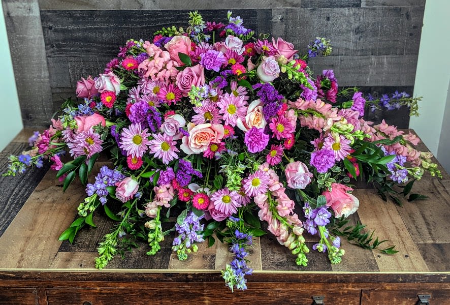 Low spray of pink and purple roses, mums, and snapdragons arranged in a wide mound.