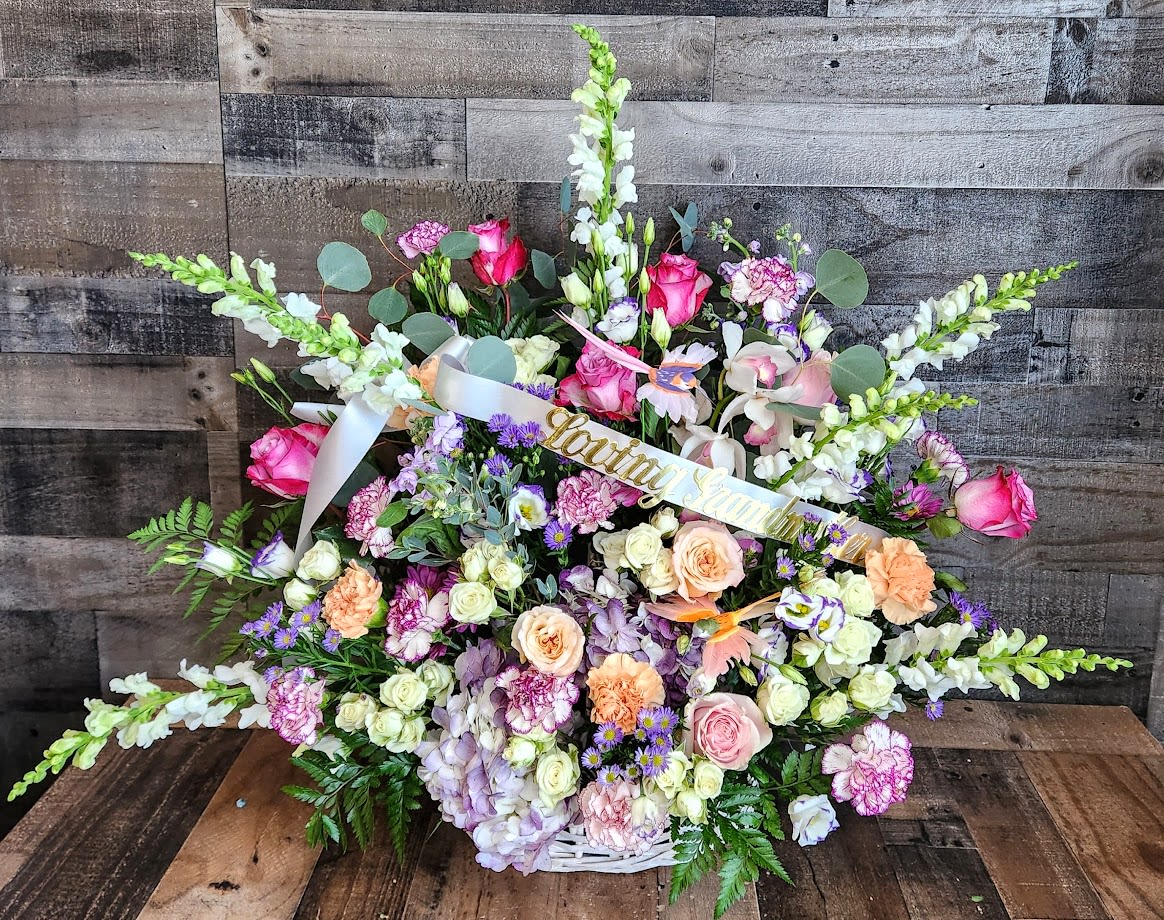 Large pastel sympathy basket with pink roses, snapdragons, and mixed flowers in a white woven basket