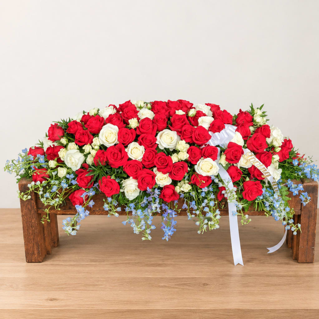 Red and white rose arrangement on a wooden bench with blue flowers