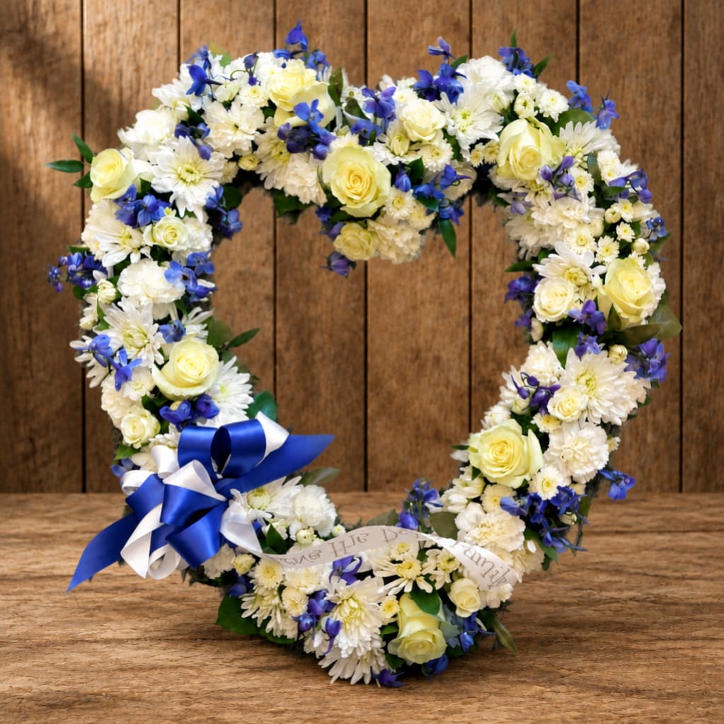 Heart-shaped floral wreath with white and yellow flowers and blue ribbon