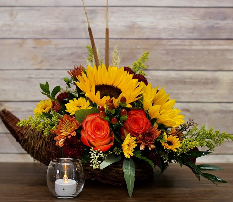 Sunflower and rose arrangement in a wicker basket with a small candle in front