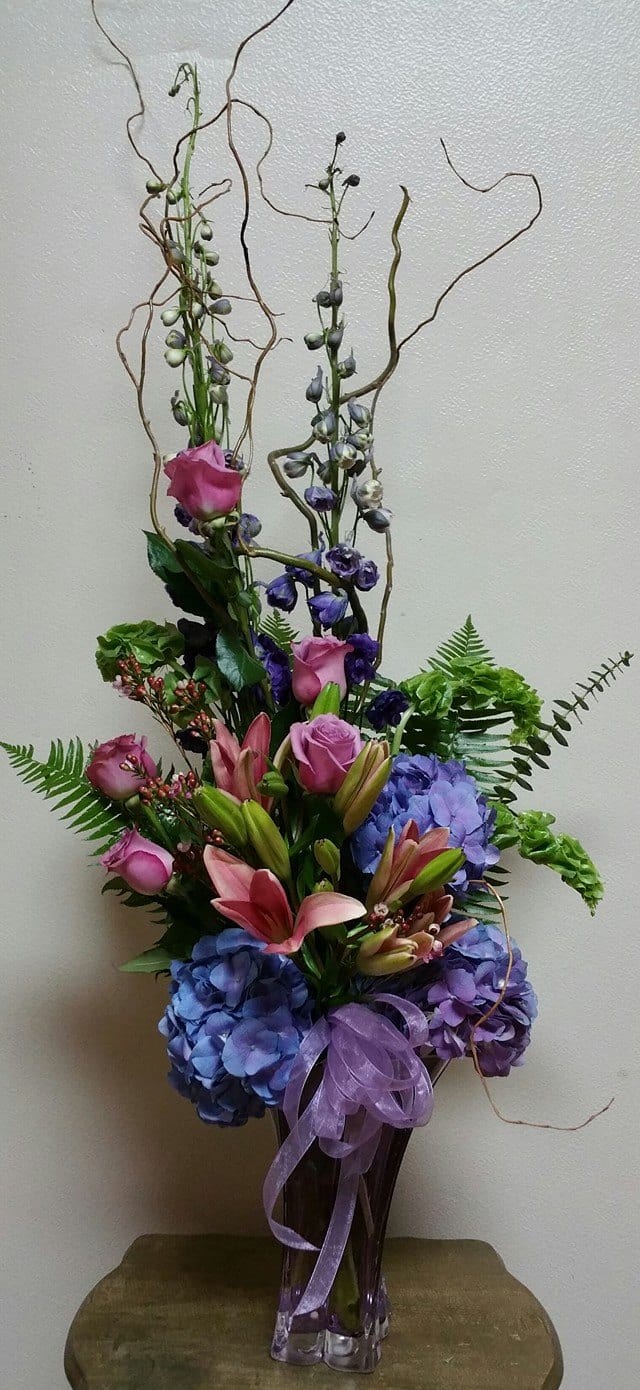 Tall bouquet of pink lilies, roses, and blue hydrangeas in a glass vase