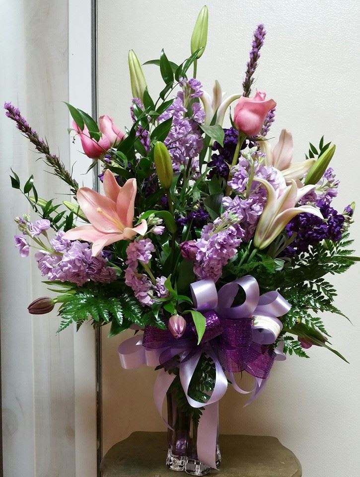 Pink lilies and purple flowers in a glass vase with a lavender ribbon