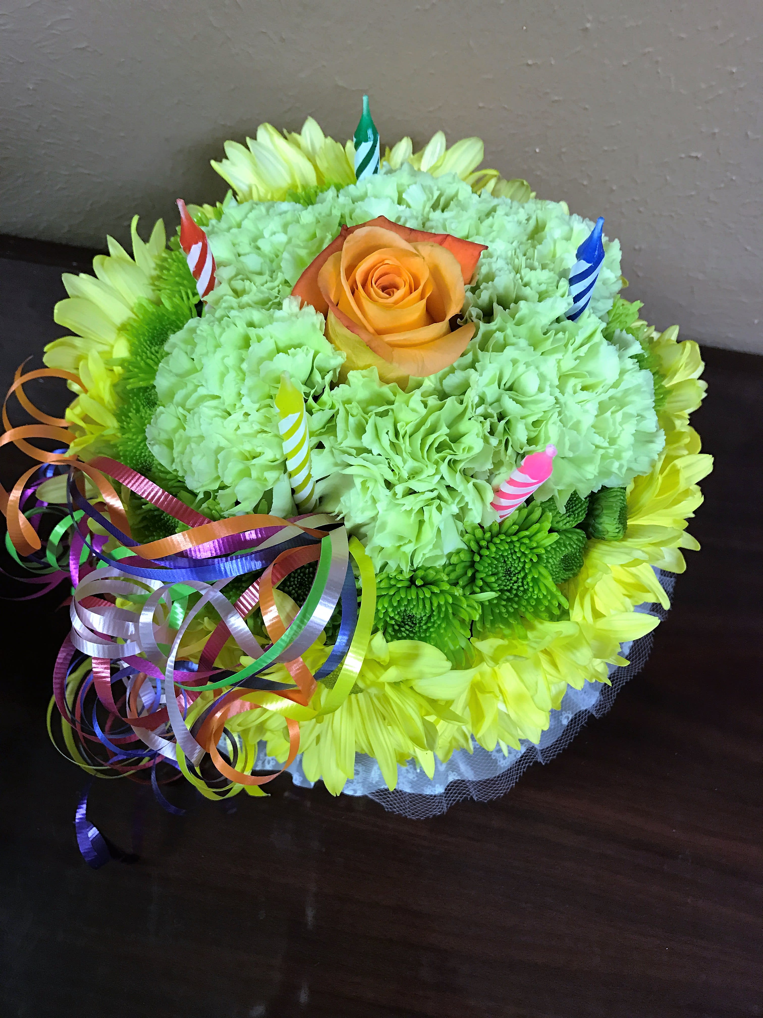 Round bouquet of green carnations and yellow daisies with an orange rose