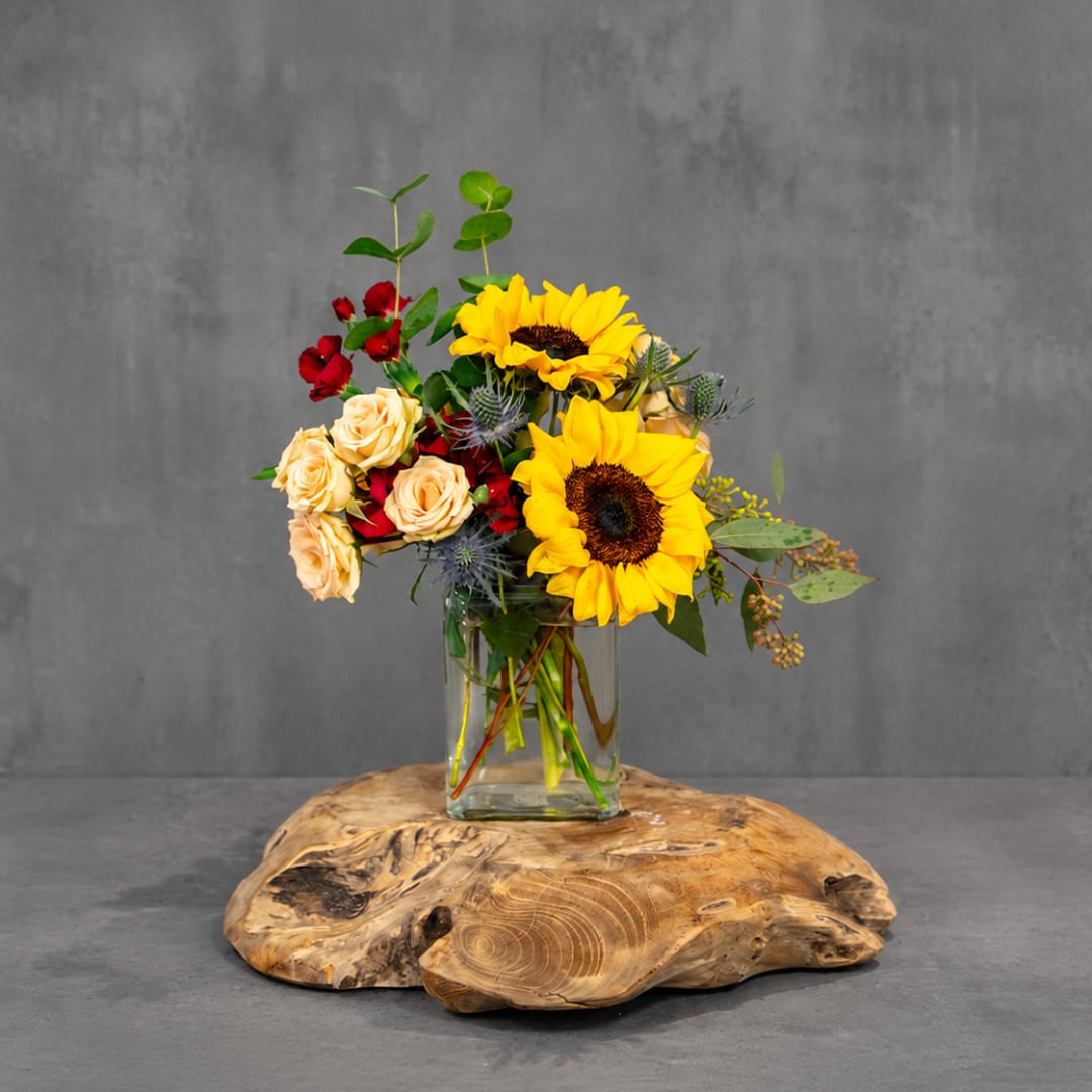 Sunflower and rose arrangement in a clear glass vase on a wooden base