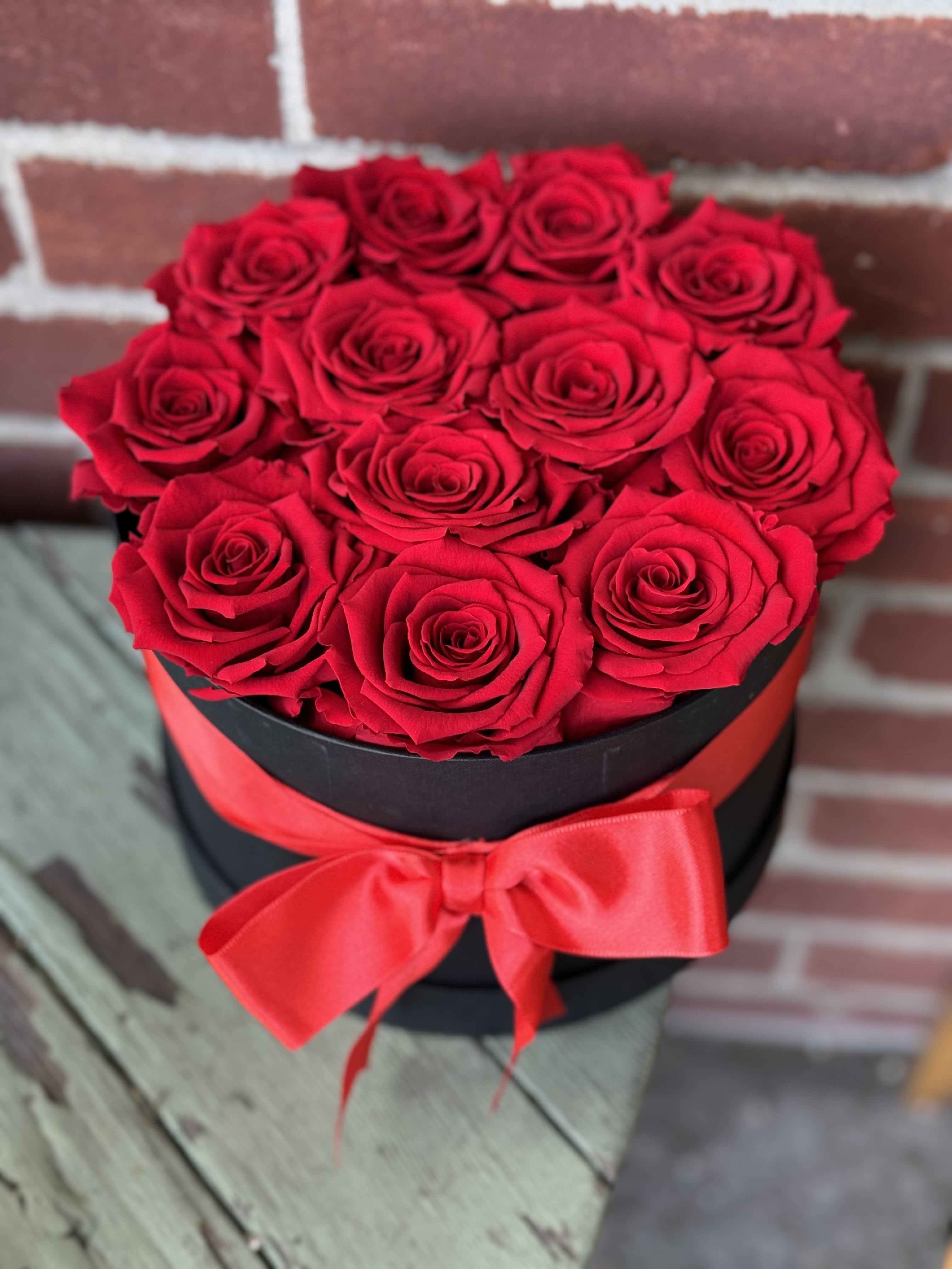Red roses arranged in a black round box with a red ribbon
