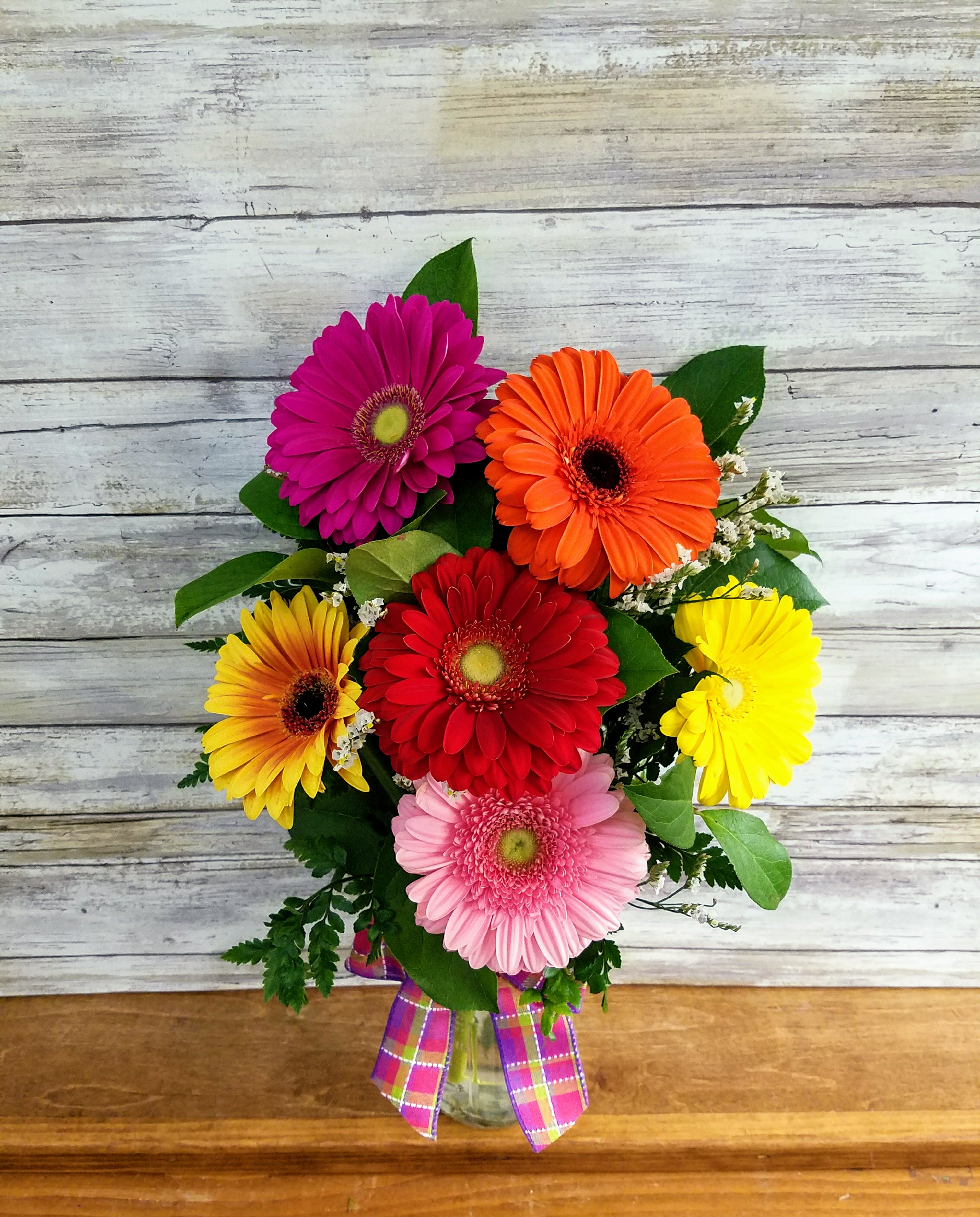 Colorful gerbera daisy bouquet in a glass vase with plaid ribbon