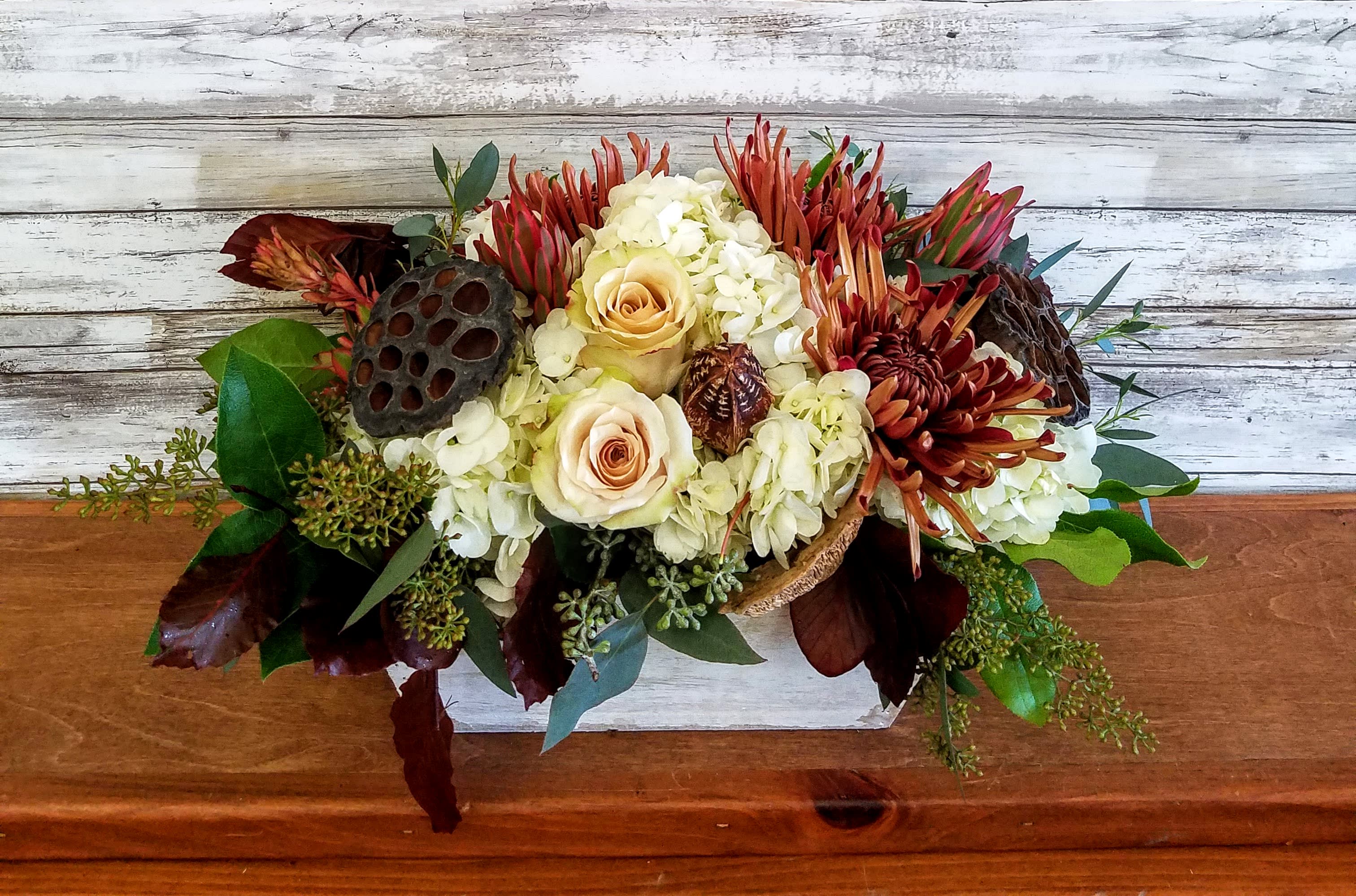Bronze Bouquet - Wow them with this seasonal arrangement of bronze and neutral tones arranged in a wooden box. White hydrangea, taupe roses, bronze mums are all accented by fall leaves, pods and seasonal greens. 