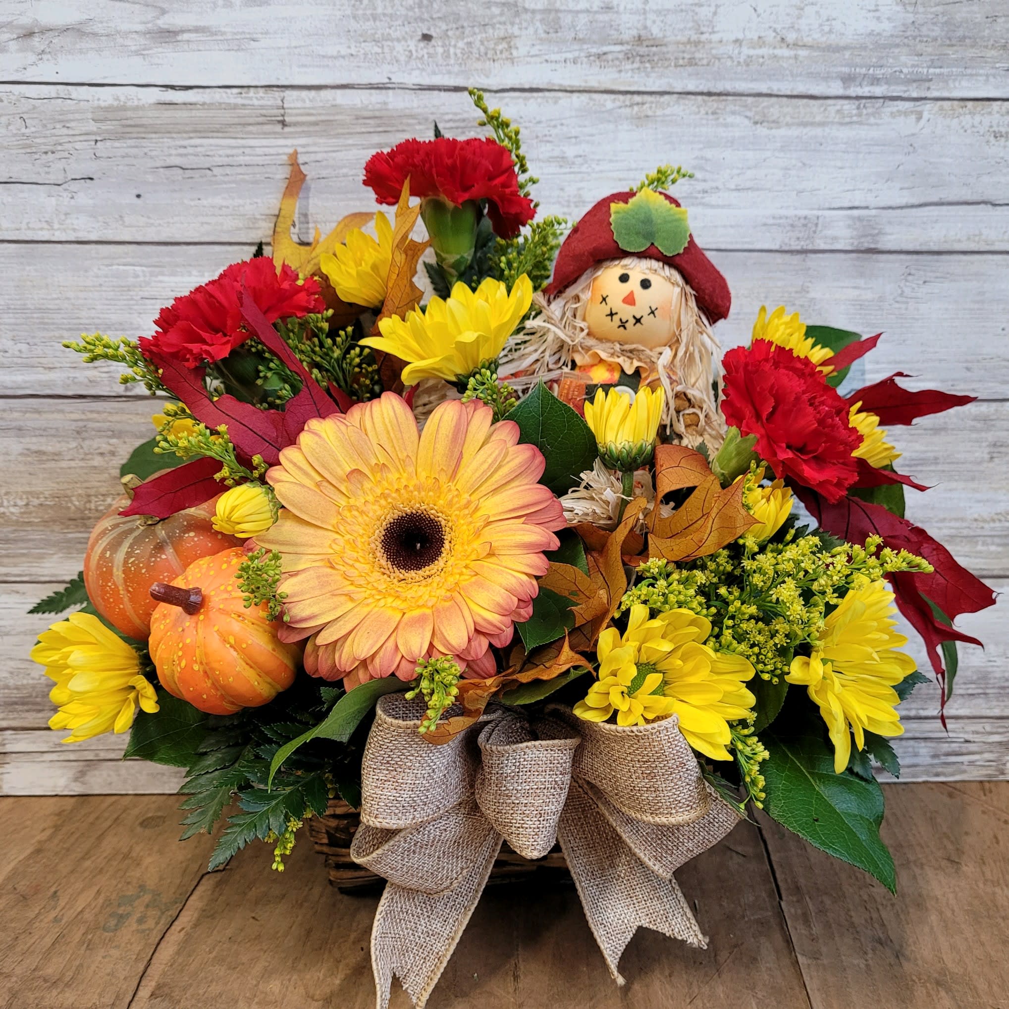Burlap and Flowers - Send this fresh fall arrangement filled with seasonal flowers and adorned with a scarecrow, pumpkins, leaves and wheat!   *Substitutions may be used based on availability 