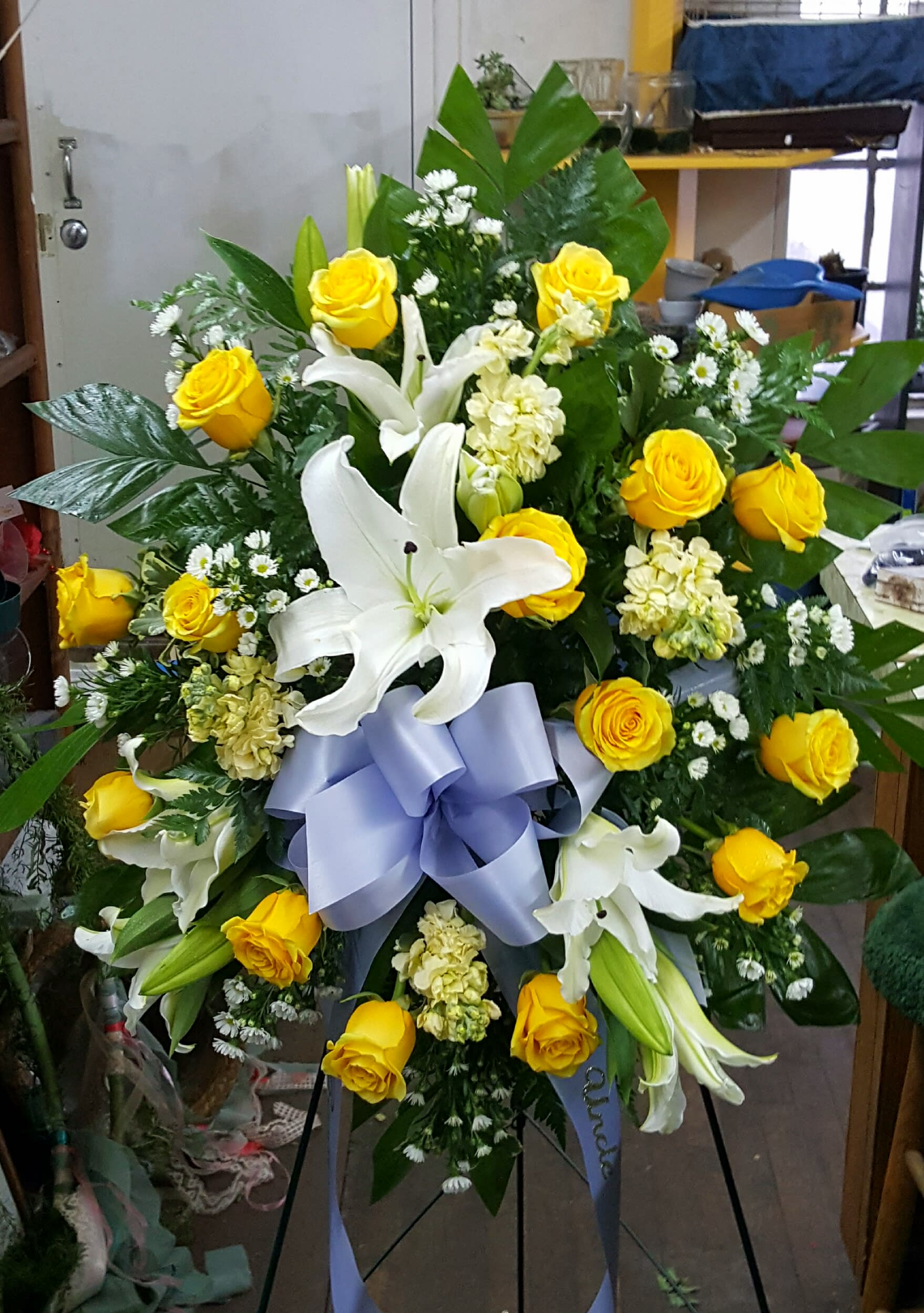 Circle Journey Easel Spray - Golden yellow roses, white lilies and butter cream stock with accent of white asters and a beautiful bow of your choice. Please call or 417 581 2328 with your choice. If preferred,  choose different colors. Approximately 30" W  x 30"H