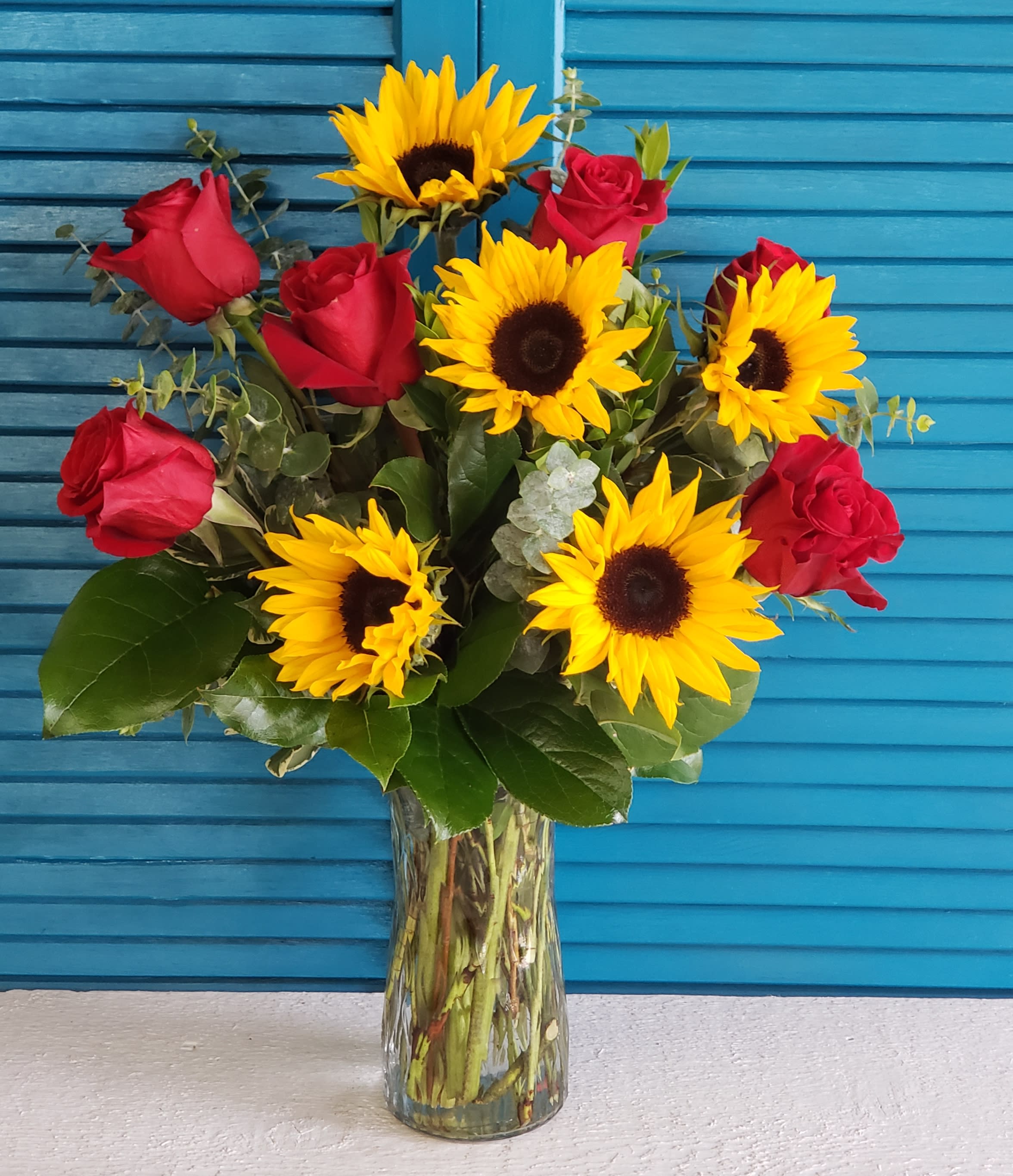 Bouquet of red roses and yellow sunflowers in a clear glass vase