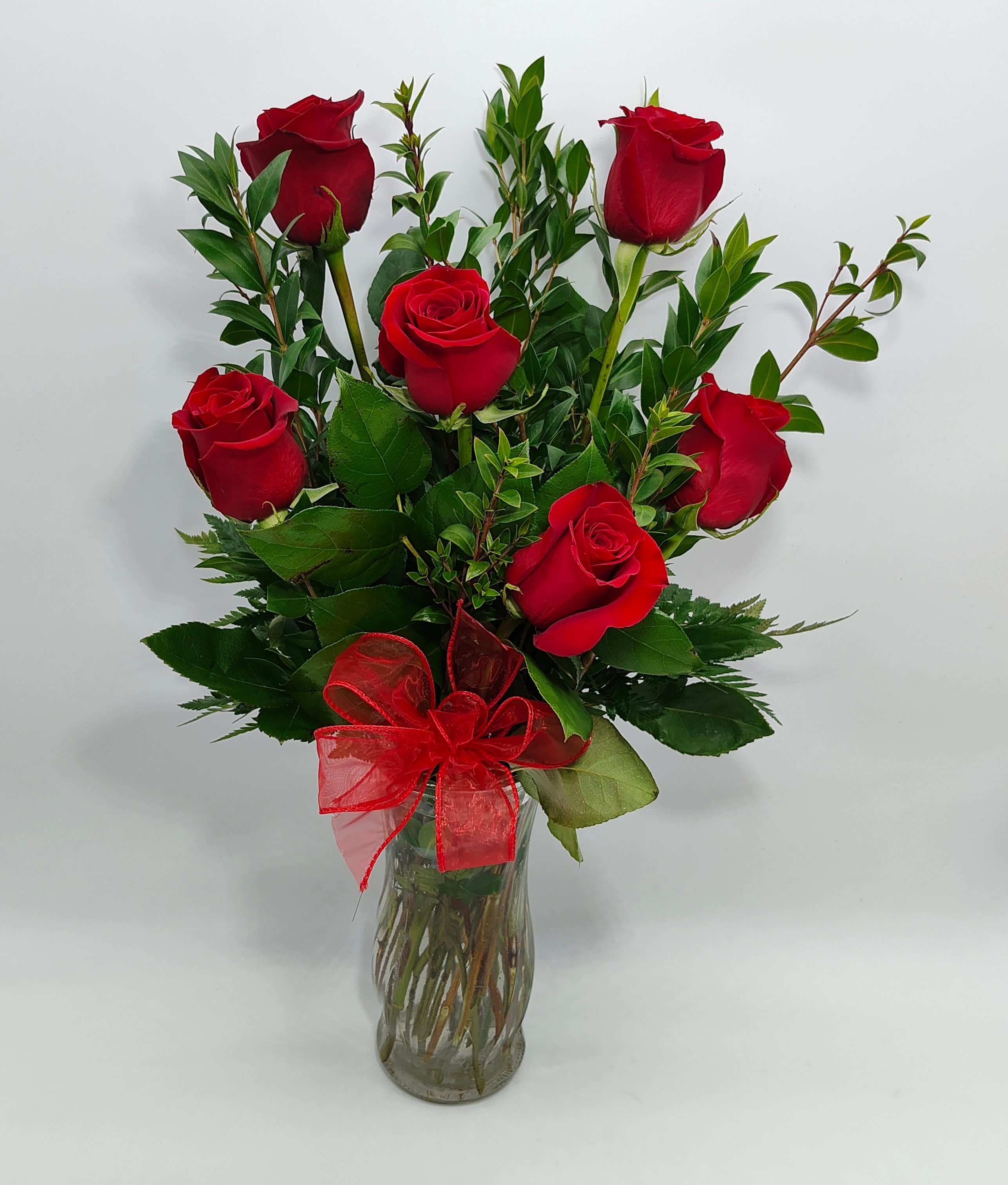 Red roses arranged in a clear glass vase with a red ribbon