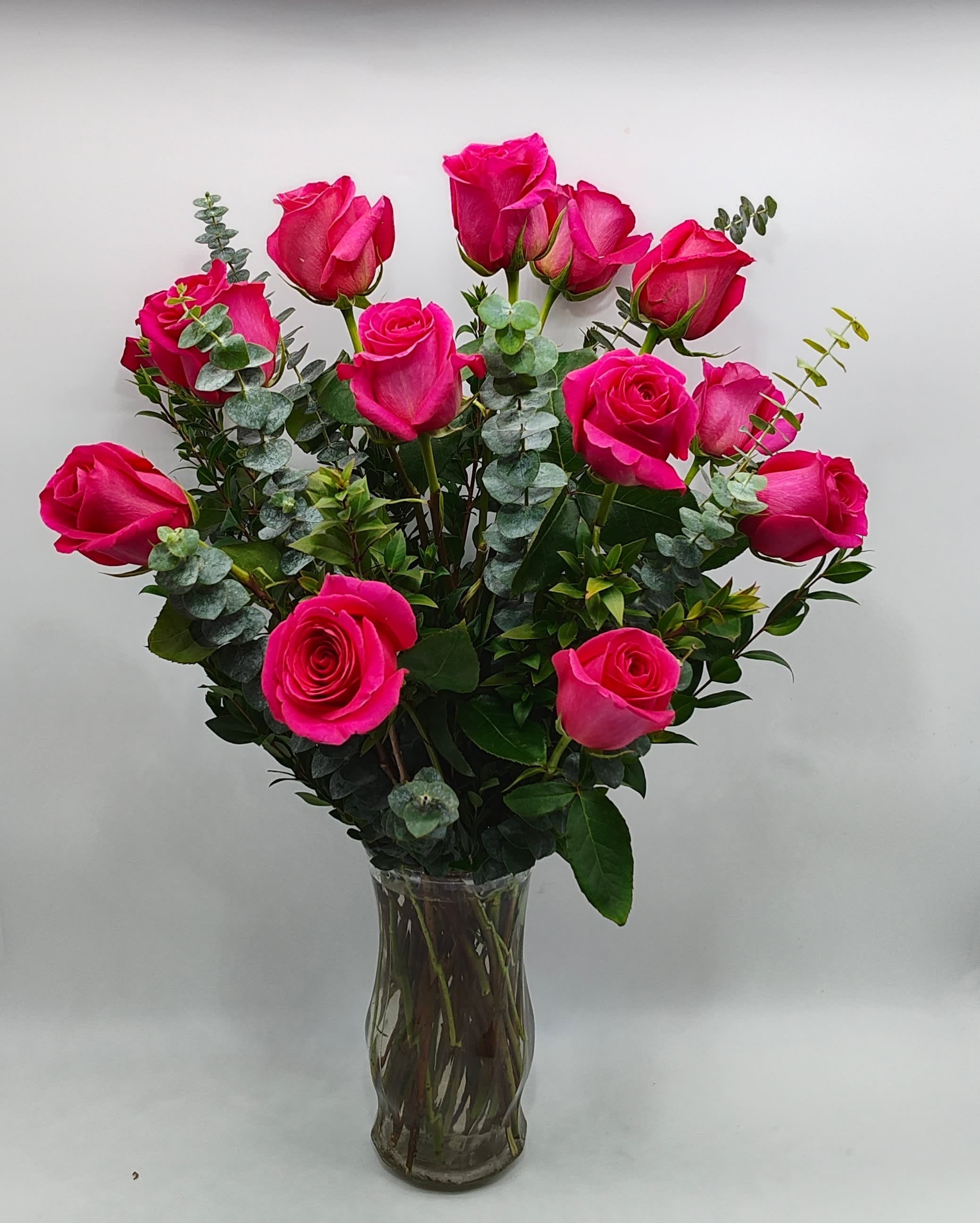 Bright pink roses arranged in a clear glass vase with eucalyptus