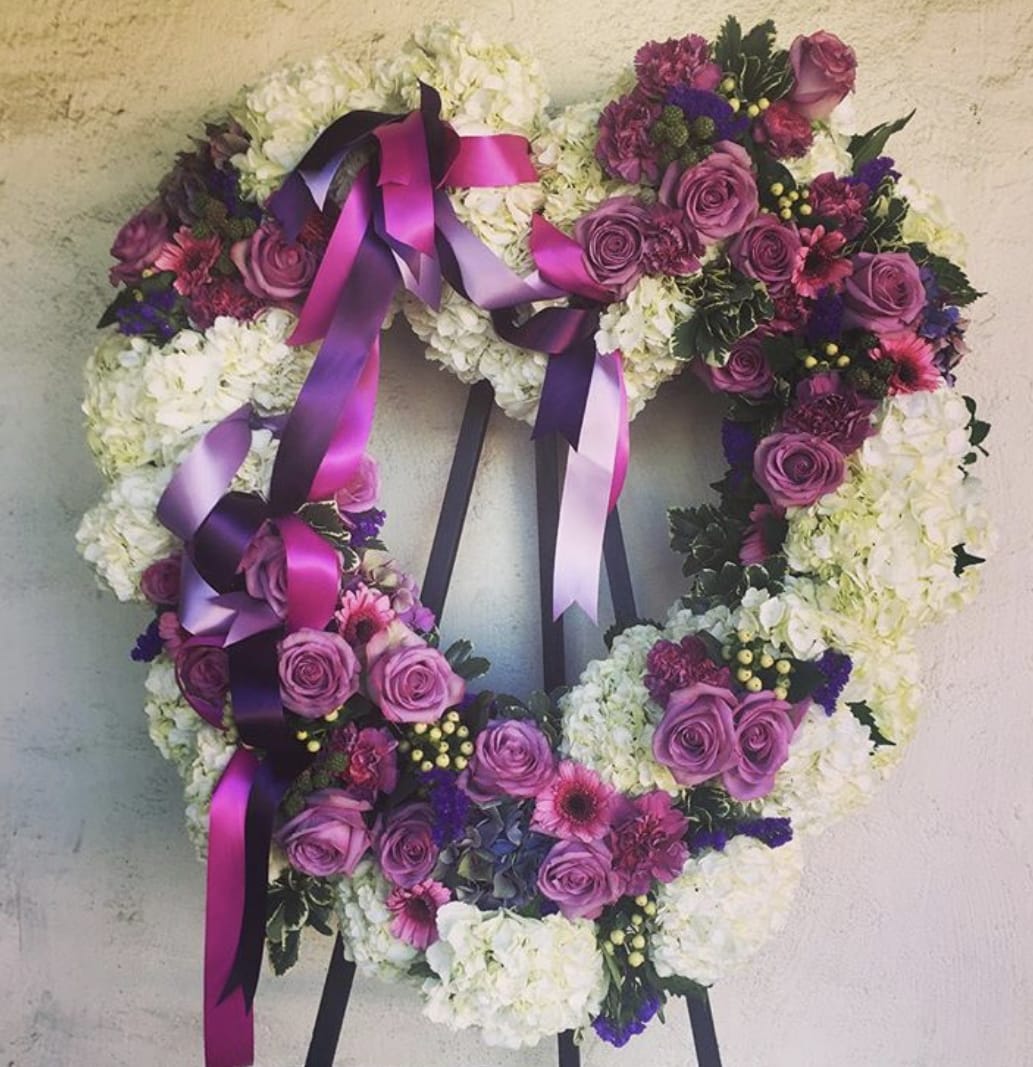 Heart-shaped floral wreath with purple roses and white blooms, tied with magenta ribbons