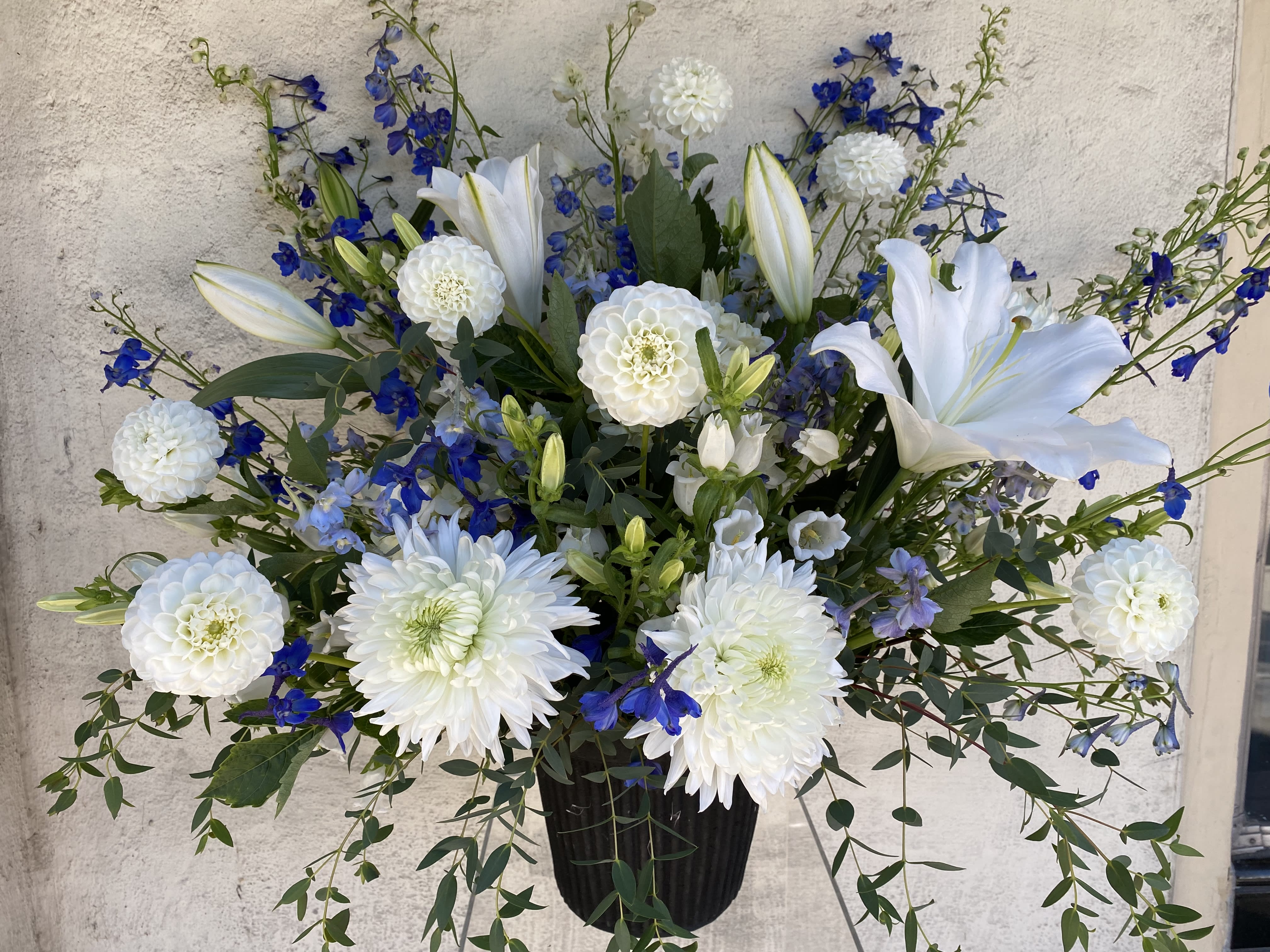 White lilies and blue flowers arranged in a black vase