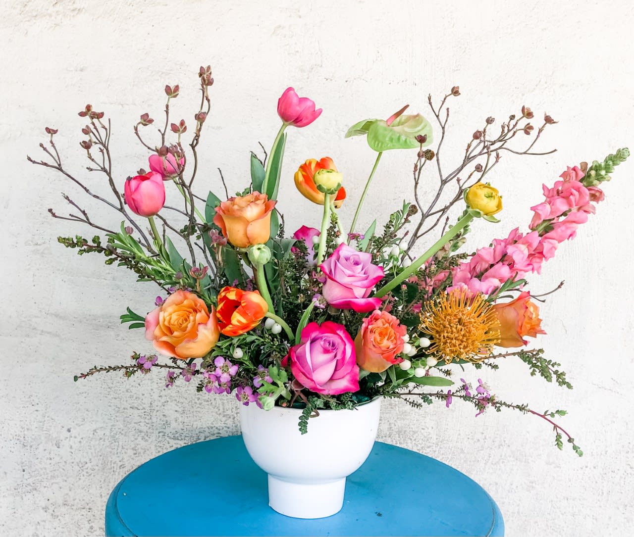 Mixed bouquet of roses, tulips, and snapdragons in a white vase