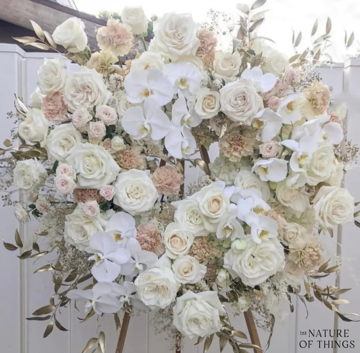 Large white floral arrangement with roses and orchids on an easel