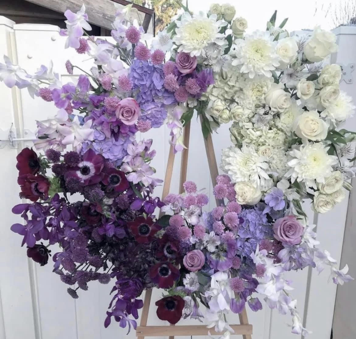 Large heart-shaped floral arrangement in purple, white, and burgundy tones on an easel