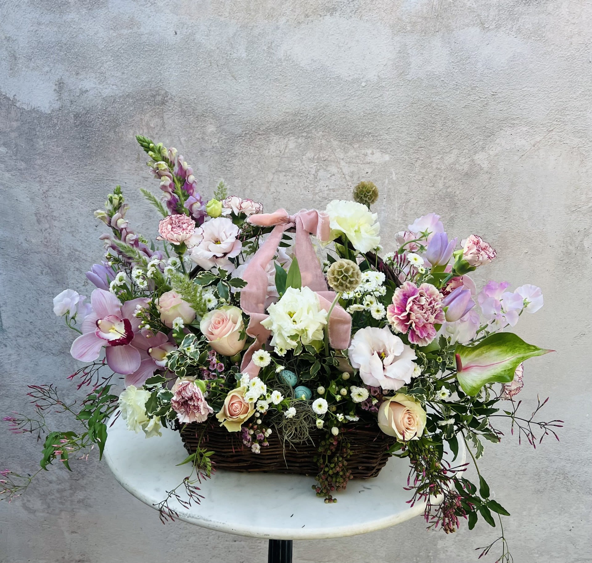 Gianna - A luxury floral arrangement designed in soft, layered shades of pink and lavender, featuring premium seasonal blooms and lush greenery. Styled in a keepsake basket, this arrangement blends natural texture with refined design for a look that feels both elevated and inviting.  Each piece is thoughtfully handcrafted using hand-selected flowers chosen for their quality, tone, and movement. The basket adds a warm, organic element, complementing the softness of the palette while creating a full, abundant presentation.  Flowers and greenery may vary due to seasonal availability, but that’s part of the charm! Our creative designers will substitute with the freshest high end product available- some grown in our very own garden!- and create something beautiful.  *Have a special request?* Let us know in the special instructions section during checkout.