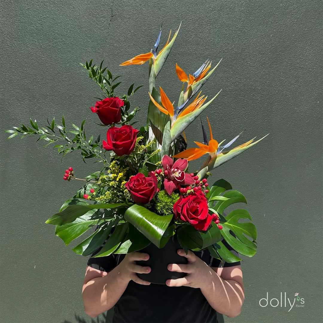 Tropical arrangement with red roses and bird-of-paradise in a black vase