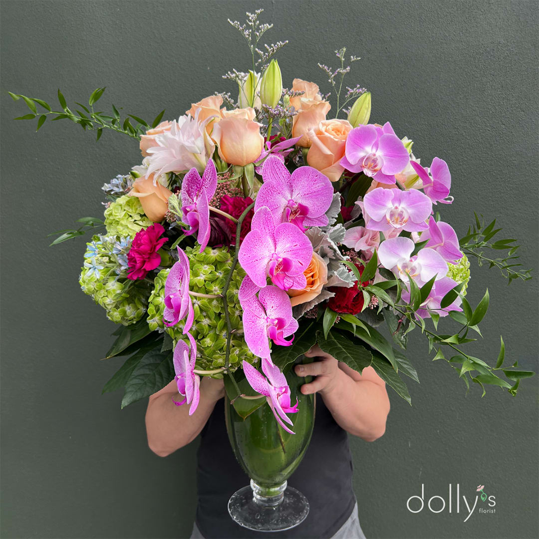 Large bouquet of pink orchids, peach roses, and green hydrangeas in a glass vase