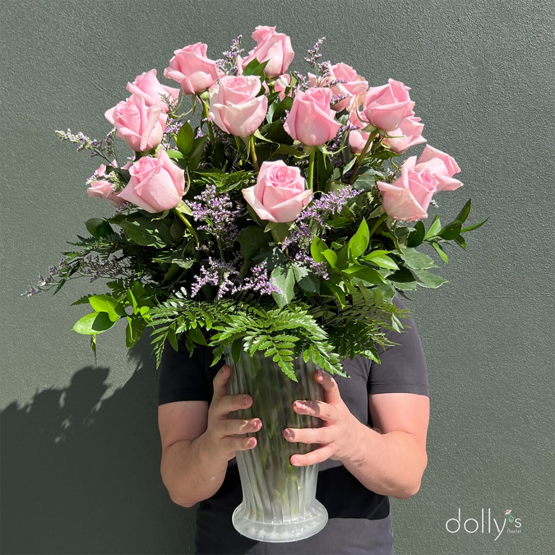 Pink roses in a clear glass vase with purple filler flowers