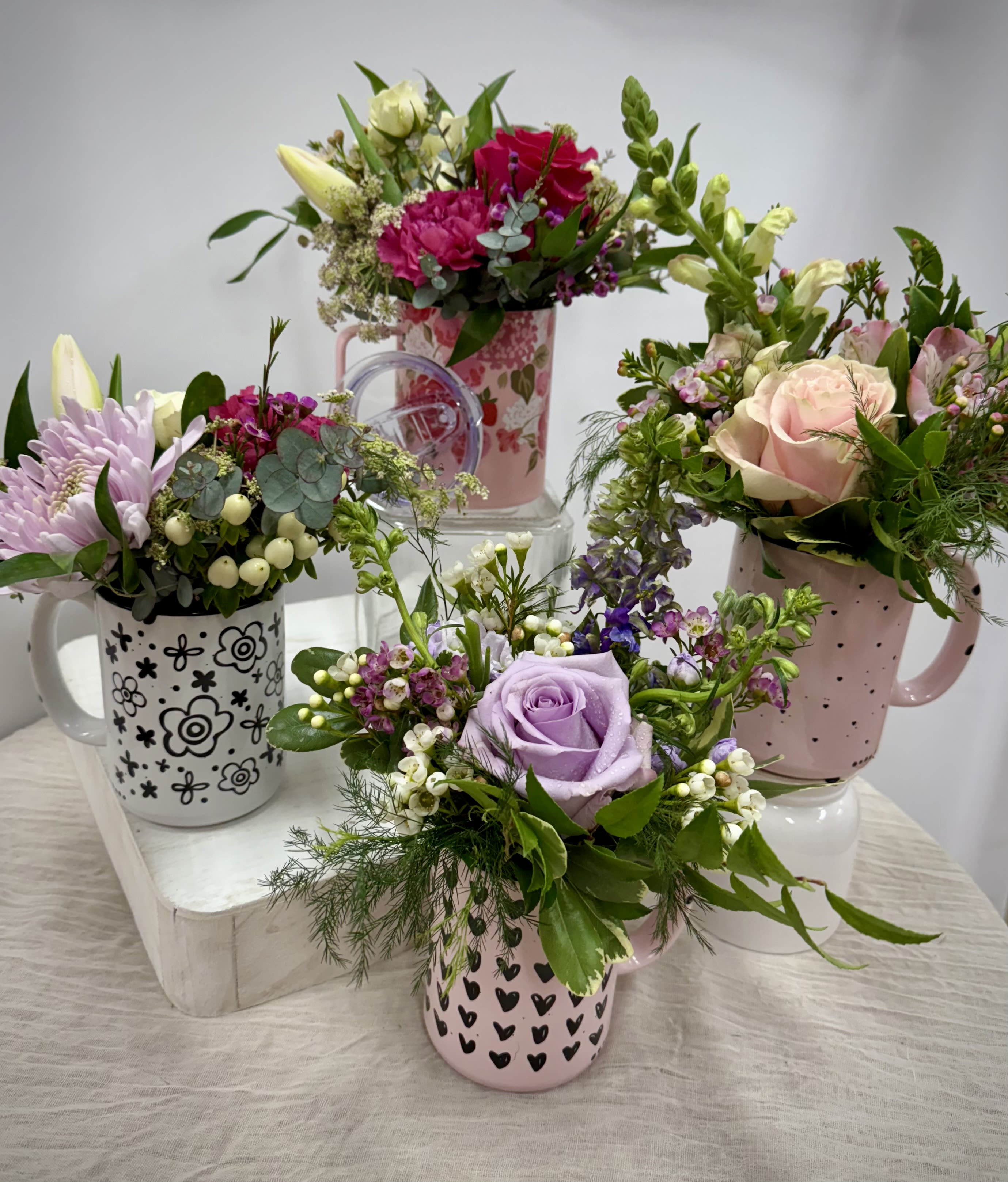 Four floral mug arrangements with roses, lilies, and mixed blooms in pastel mugs.