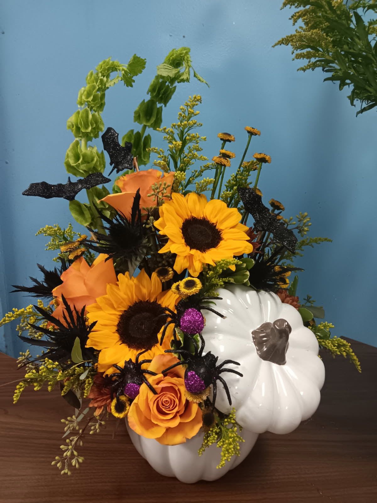 Orange and yellow floral arrangement in a white pumpkin container with black spider decorations
