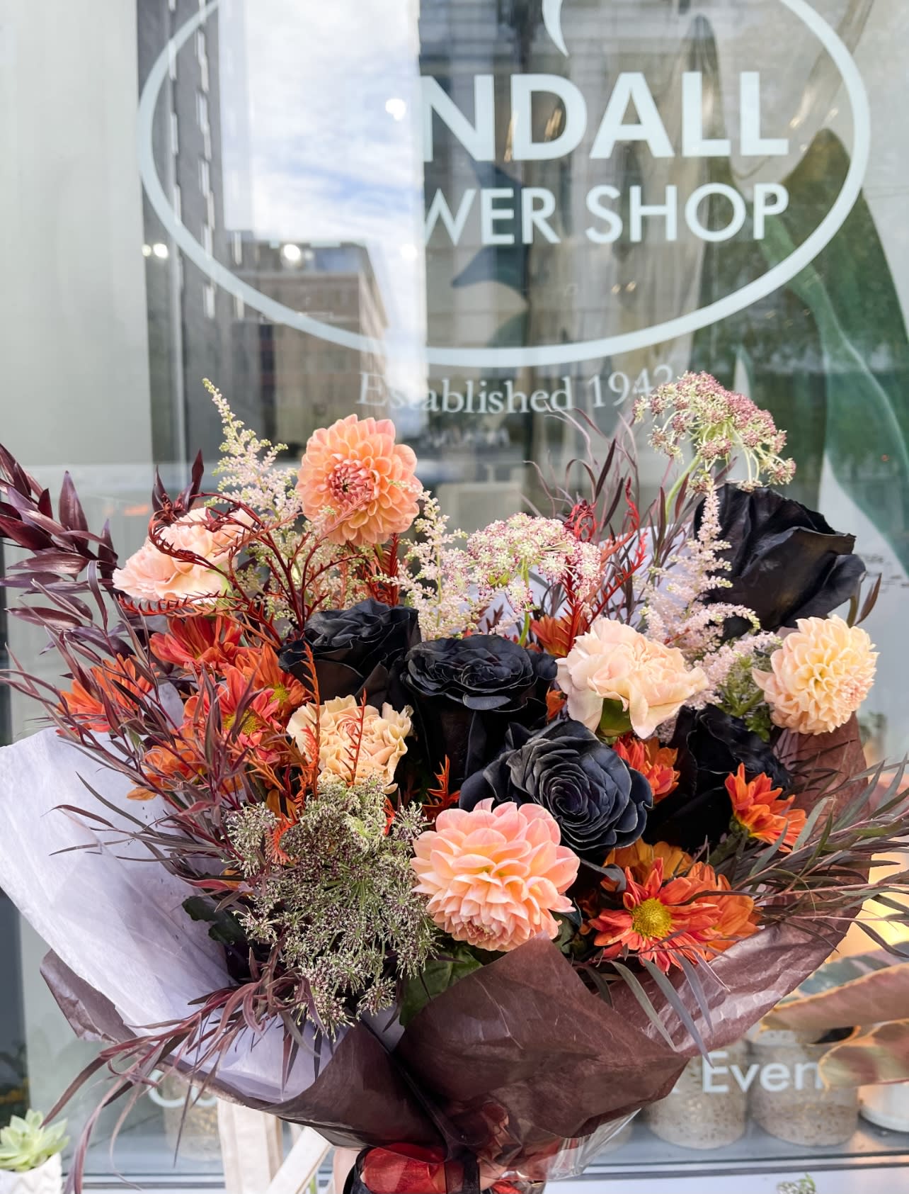 Bouquet of peach, orange, and black flowers wrapped in dark paper