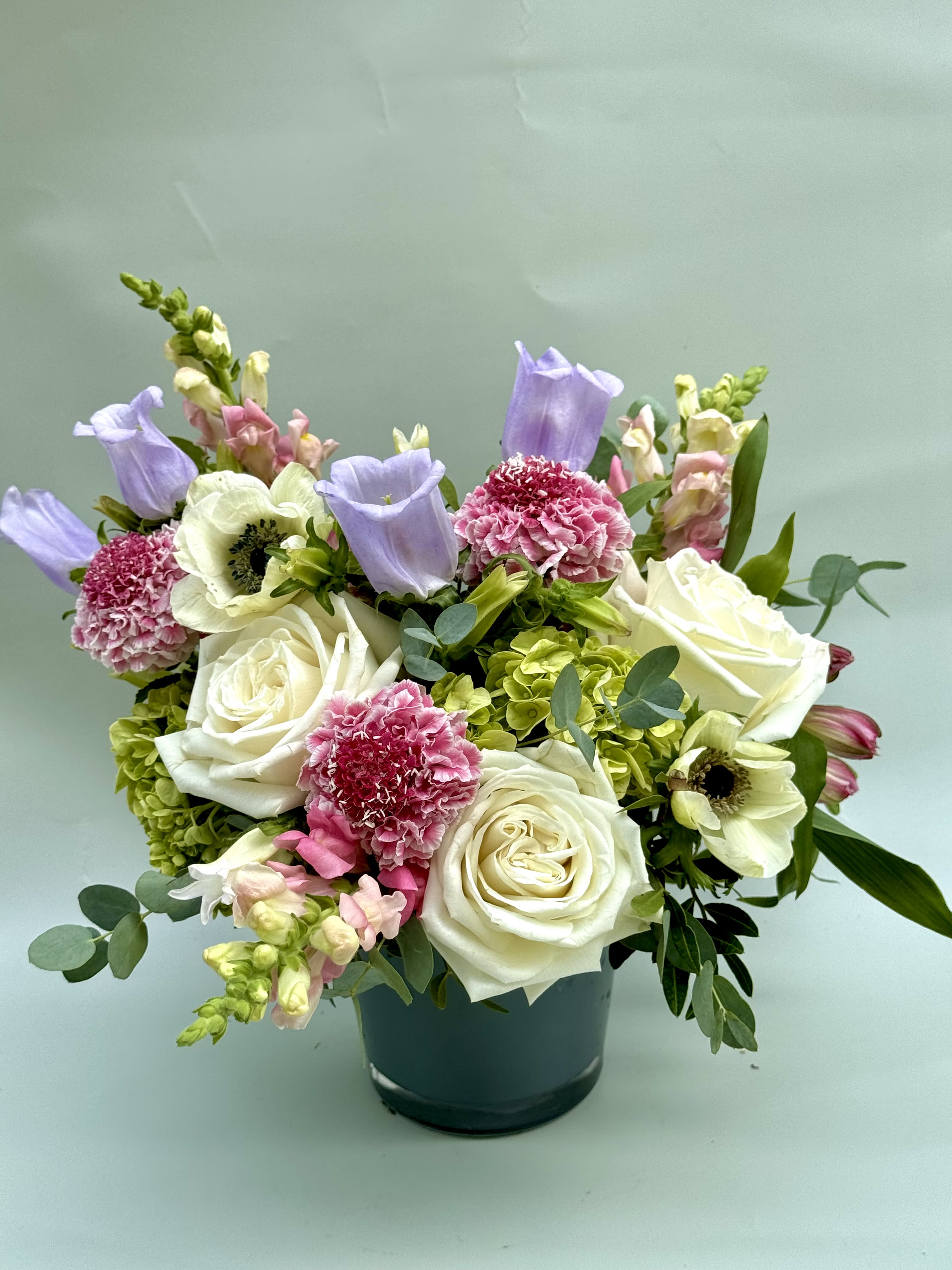 Mixed bouquet of white roses, pink carnations, and lavender blooms in a dark vase