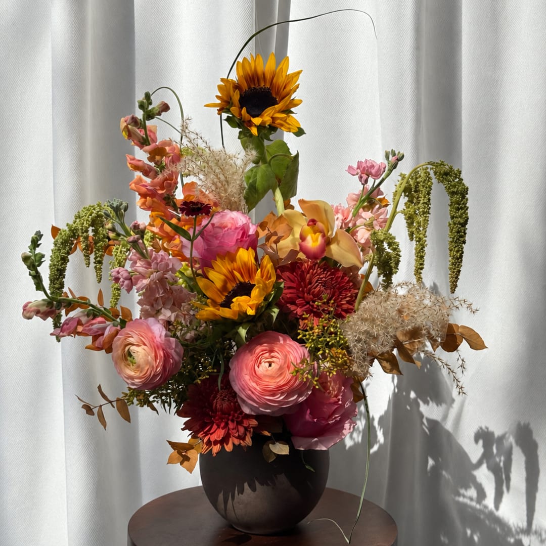 Mixed bouquet in a dark vase with sunflowers, pink blooms, and orange flowers