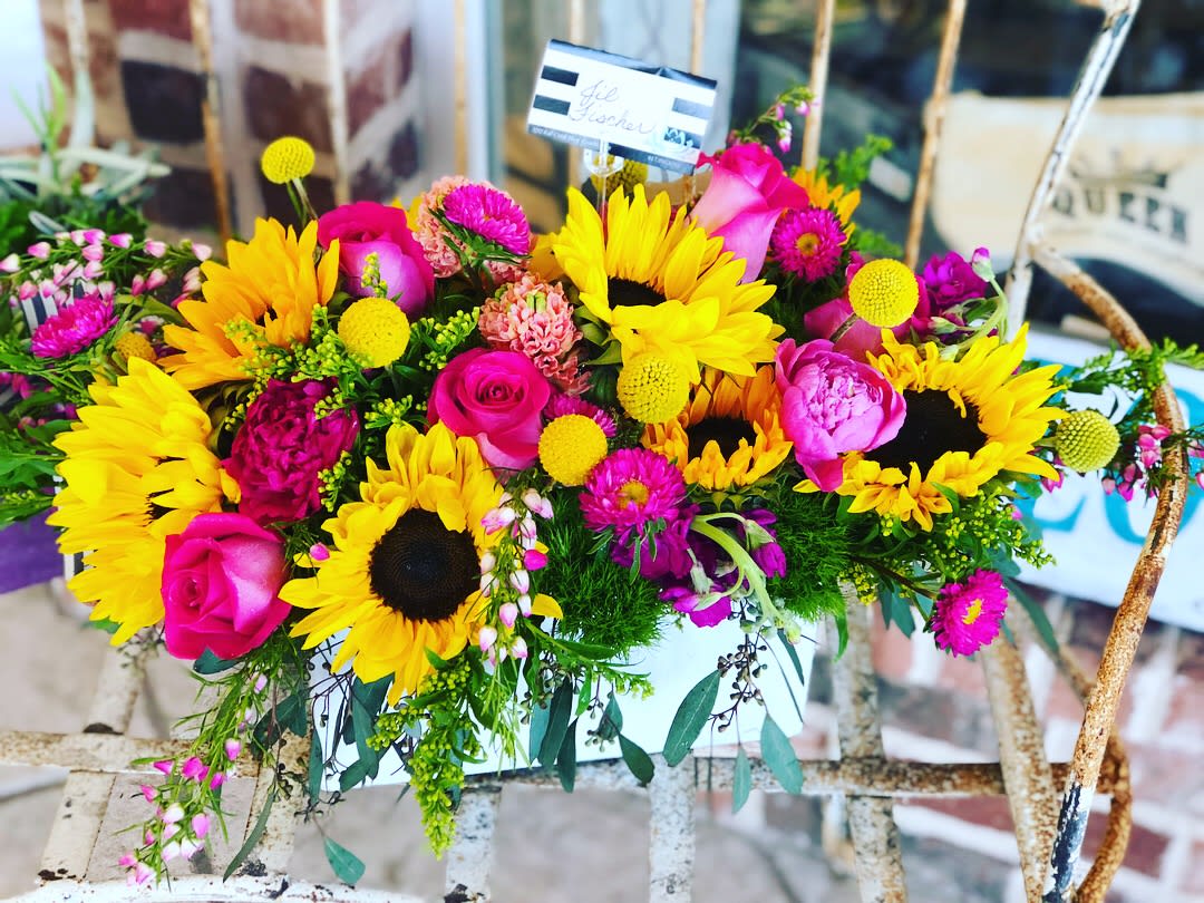 Bright bouquet with sunflowers, pink roses, and magenta flowers in a white container