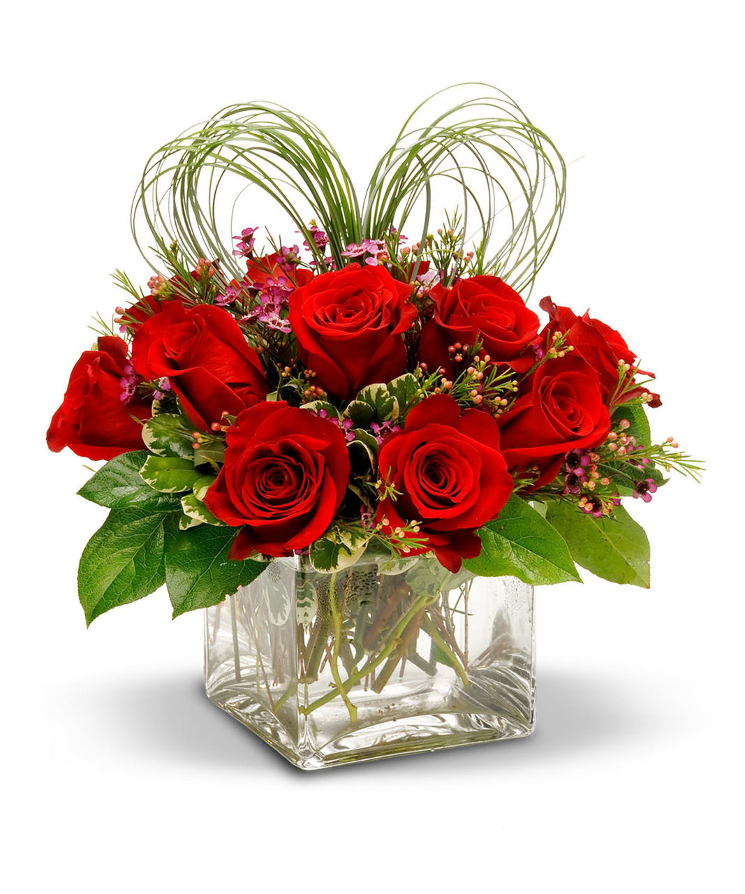 Red roses arranged in a clear square vase with looping grass accents