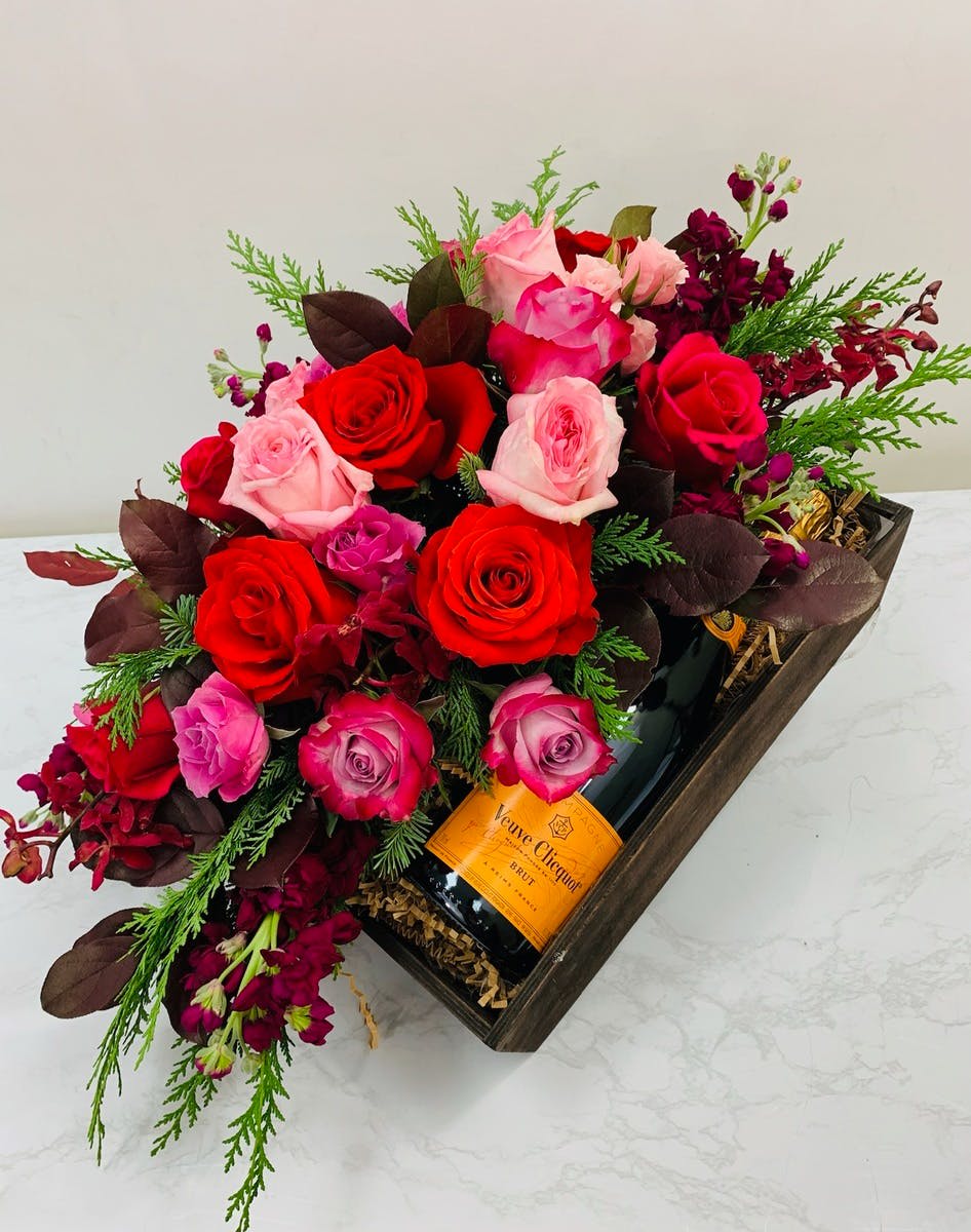 Red and pink roses arranged in a gift box with a champagne bottle