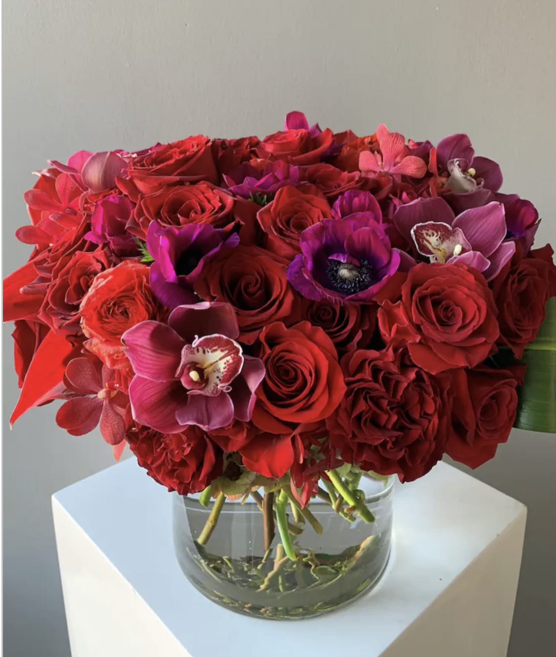 Red and pink bouquet of roses and orchids in a clear glass vase