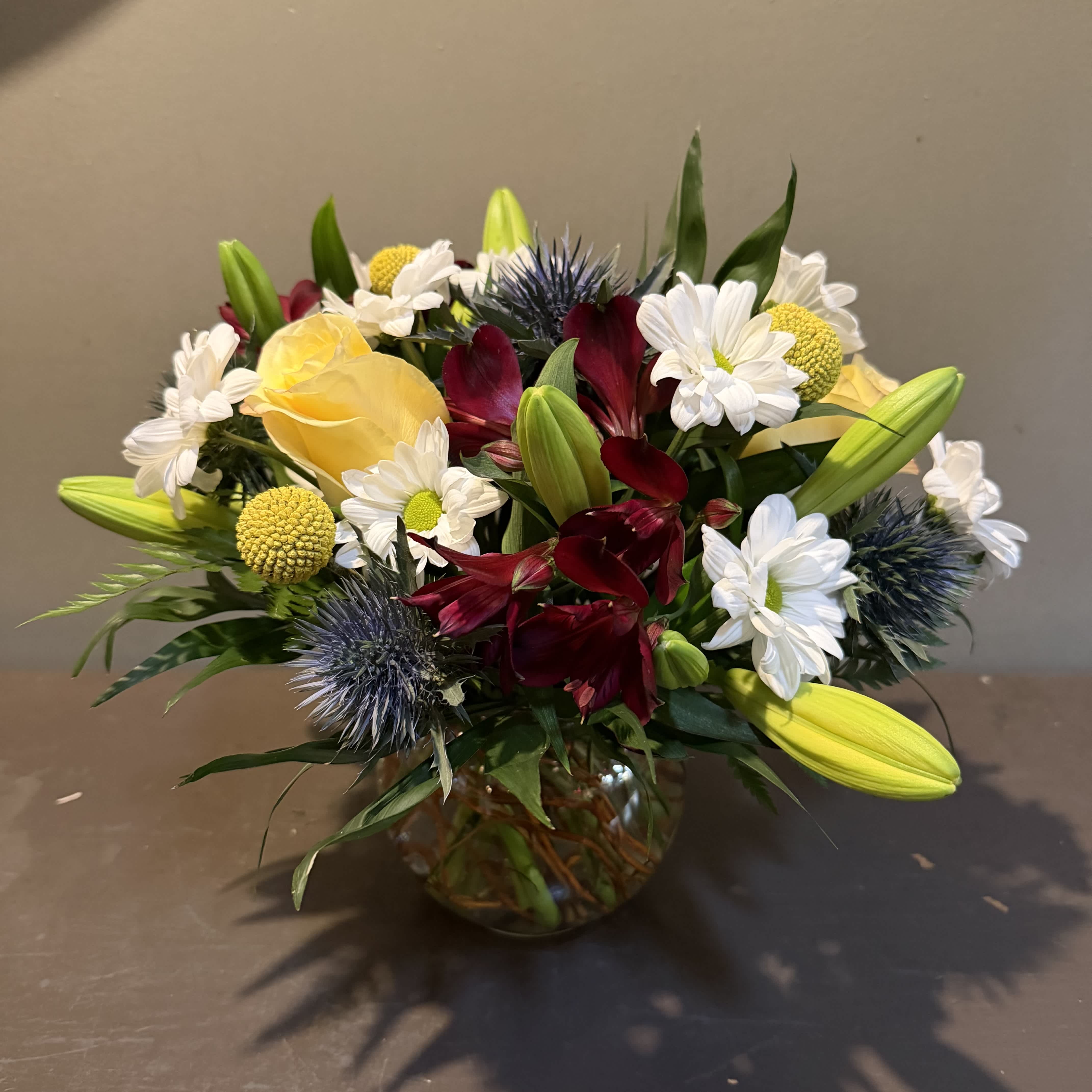 Bouquet of yellow roses, white daisies, and burgundy flowers in a glass vase