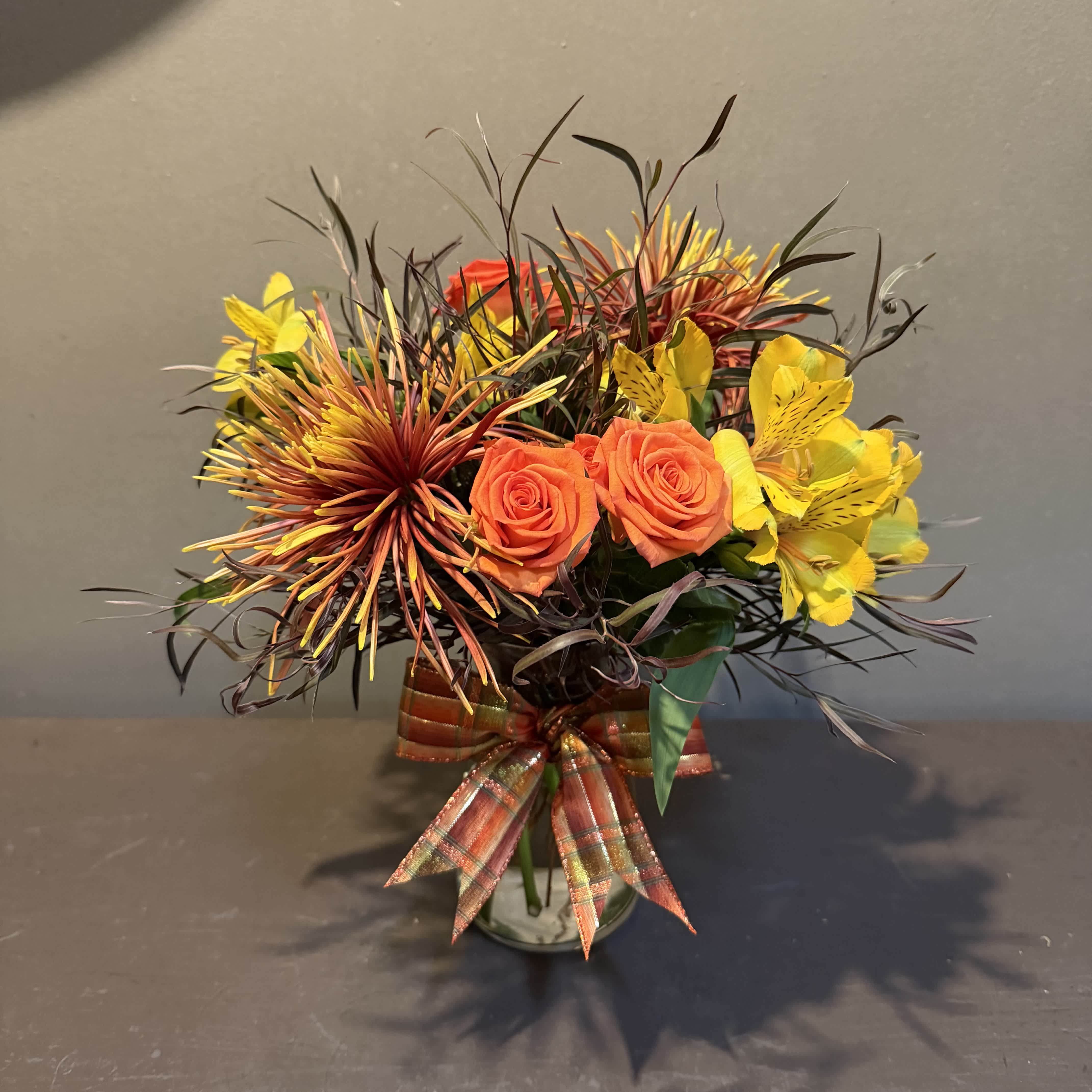 Orange roses and yellow alstroemeria in a glass vase with a plaid ribbon