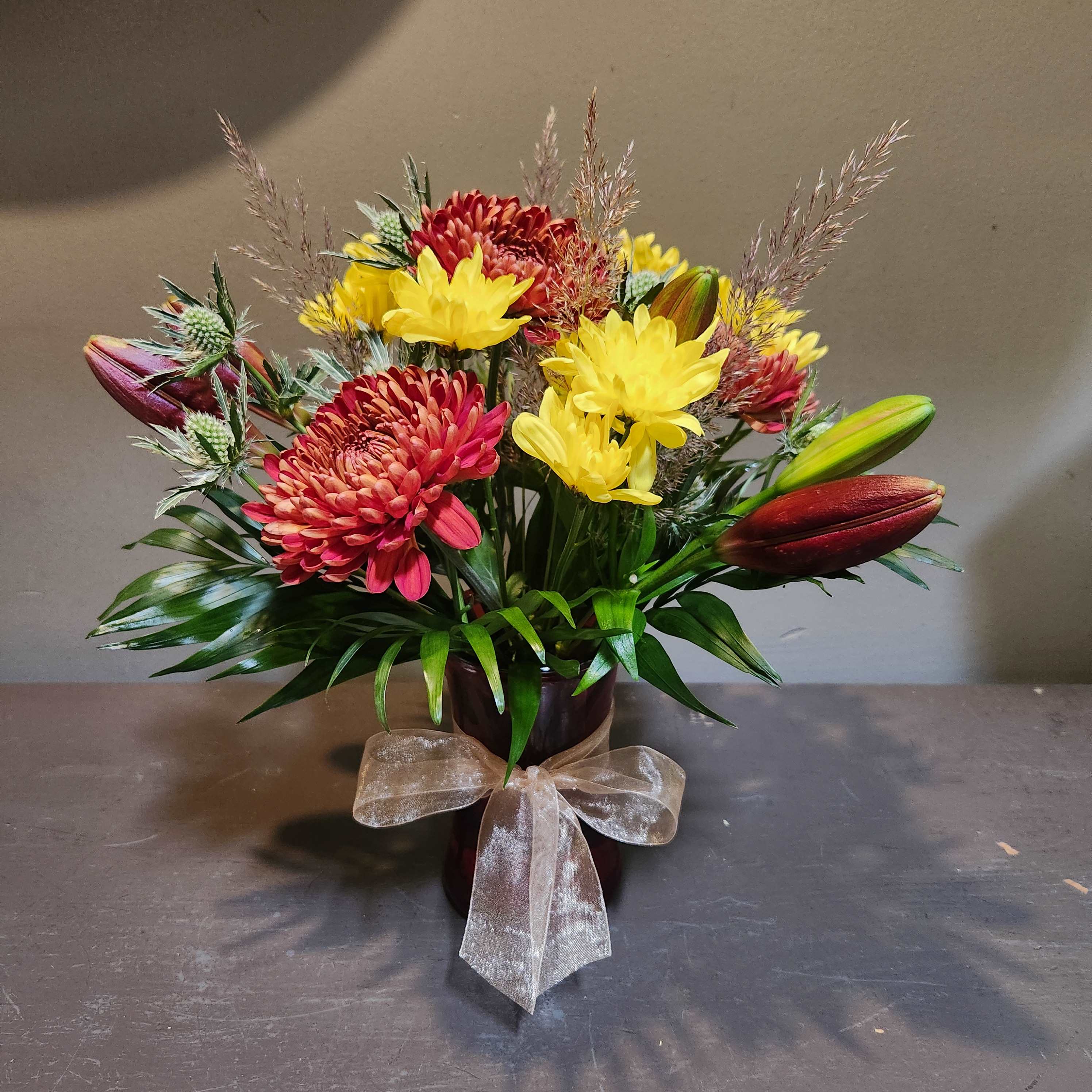 Bouquet of red and yellow flowers in a dark vase with a sheer bow