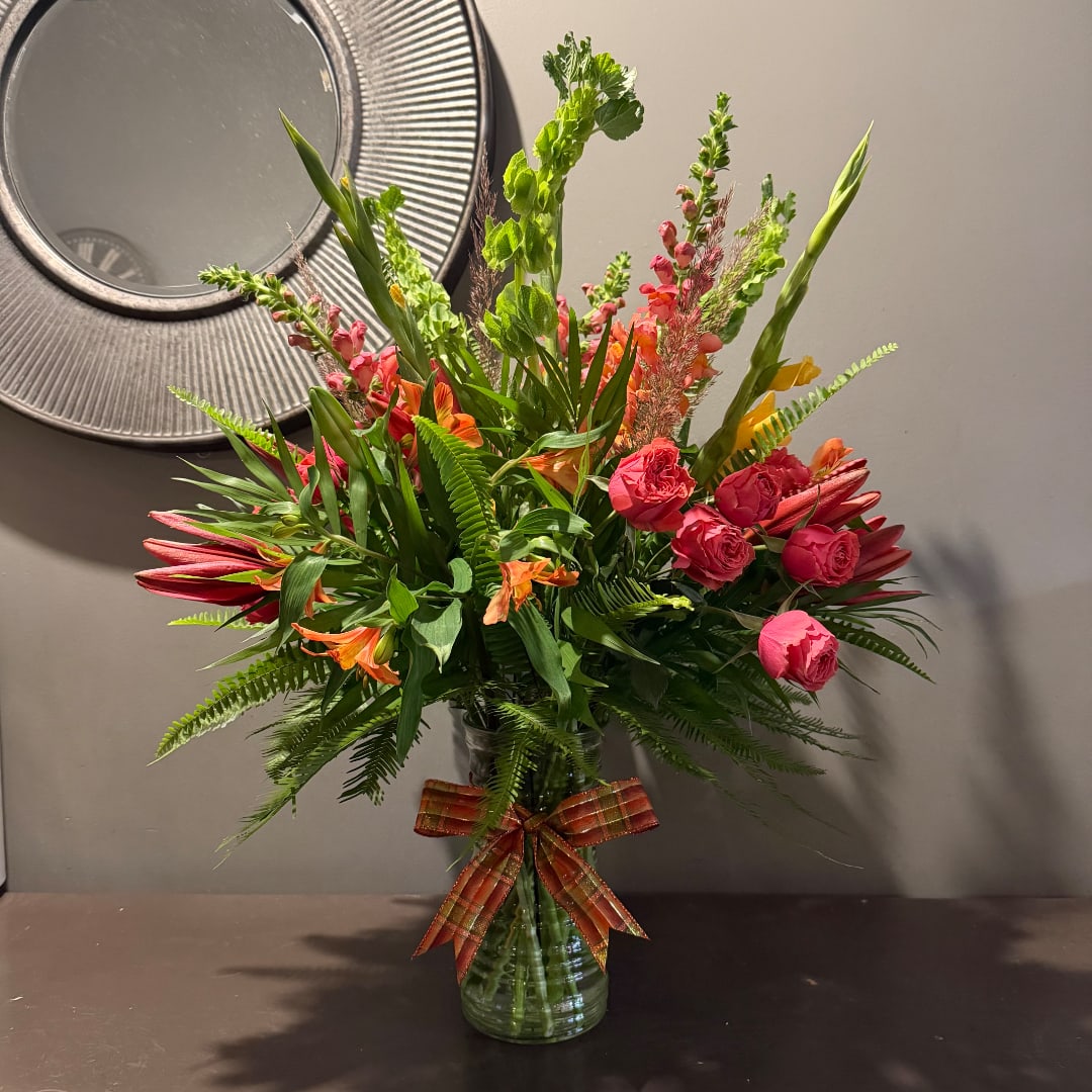 Mixed bouquet of pink and orange flowers in a glass vase with a plaid ribbon