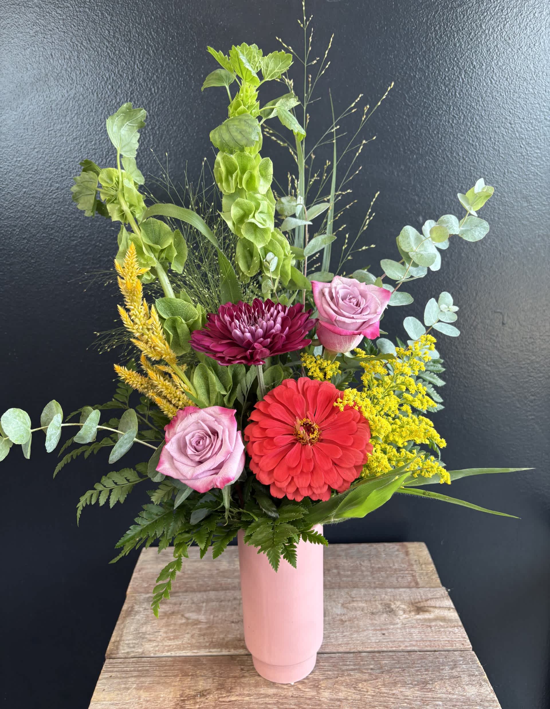 Mixed bouquet in a pink vase with roses, a red zinnia, and yellow filler flowers